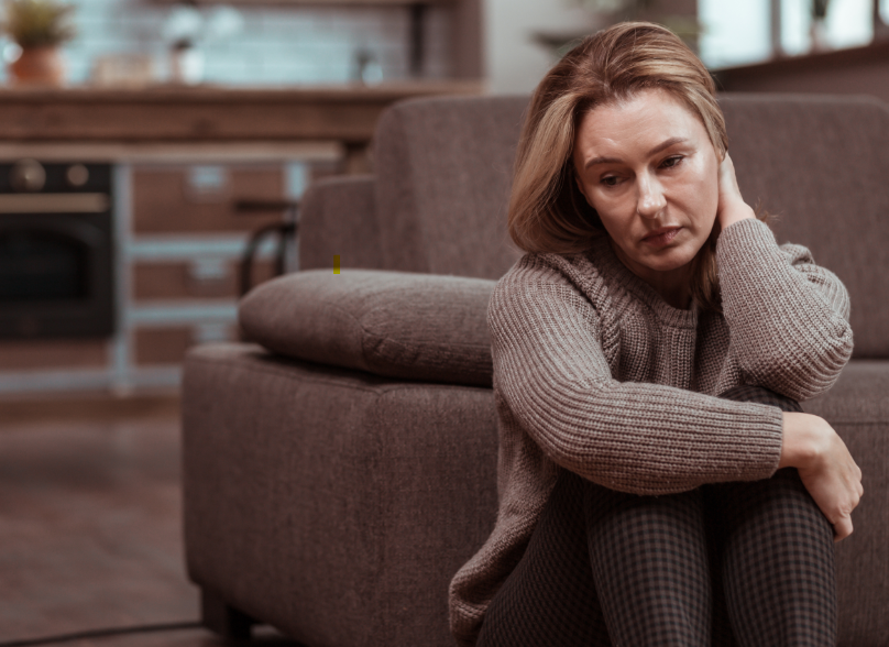 Woman sitting in front of couch looking depressed